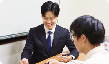 机を挟んで笑顔で生徒と話すスーツ姿の男性講師