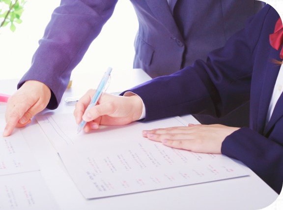 プリントにペンで書き込む制服姿の生徒とサポートする手元