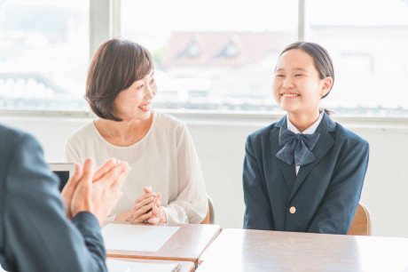 教室で保護者と並んで笑顔で話を聞く制服姿の女子生徒