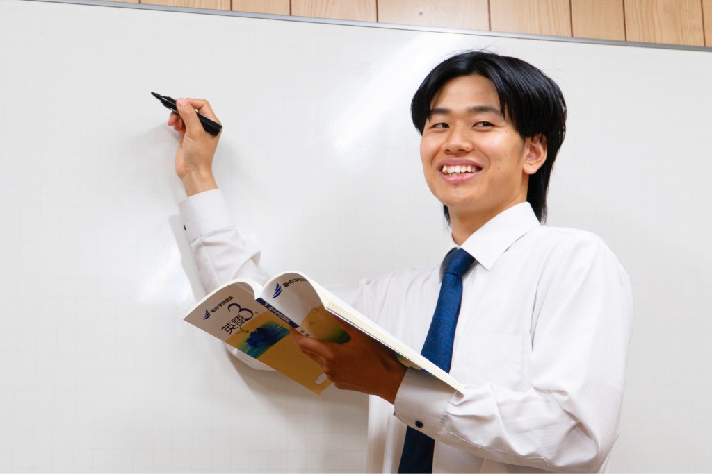 ホワイトボードの前で教科書を手に笑顔で解説する男性講師