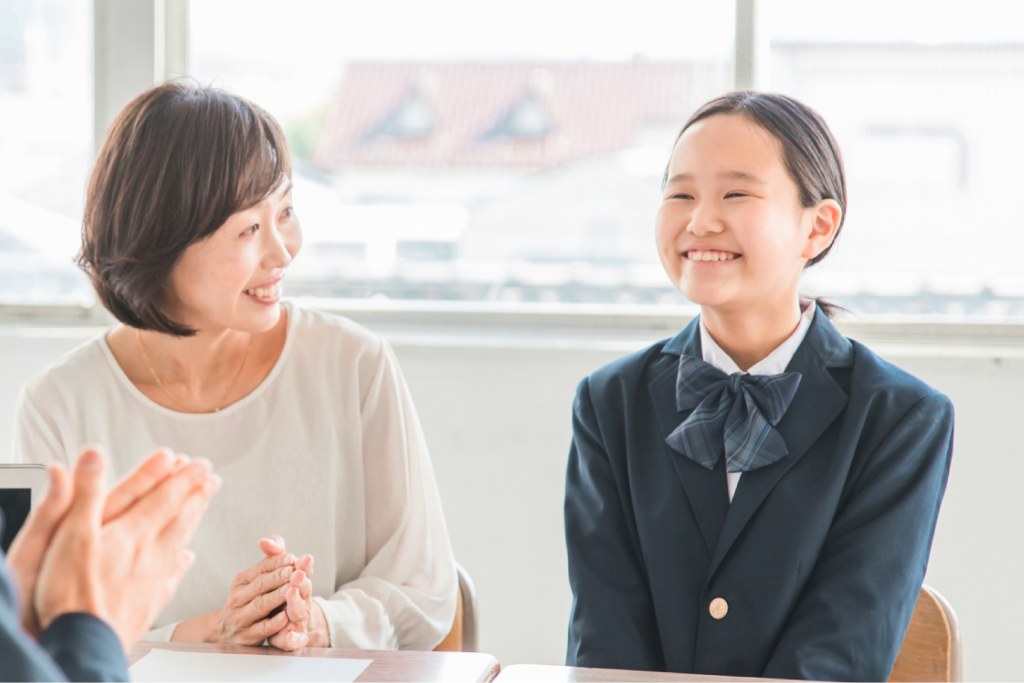 教室で笑顔で向かい合って面談する保護者と制服姿の女子生徒