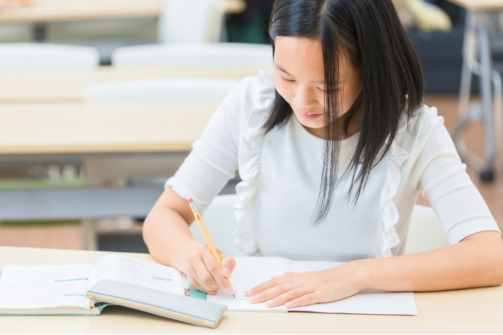 教室の机で鉛筆を握りノートに向かう女子生徒