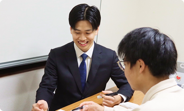 机を挟んで笑顔で生徒と話すスーツ姿の男性講師